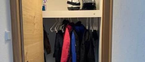 A narrow hallway leading to a closet with hanging clothes and shoes.