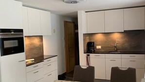 A compact kitchen with white cabinets, a black oven, and a dining table with floral tablecloth. - Elena # 2 Appartement/Fewo, Dusche oder Bad, WC, 1 Schlafraum 2-Bett-Wohnung by Interhome (Lenk)