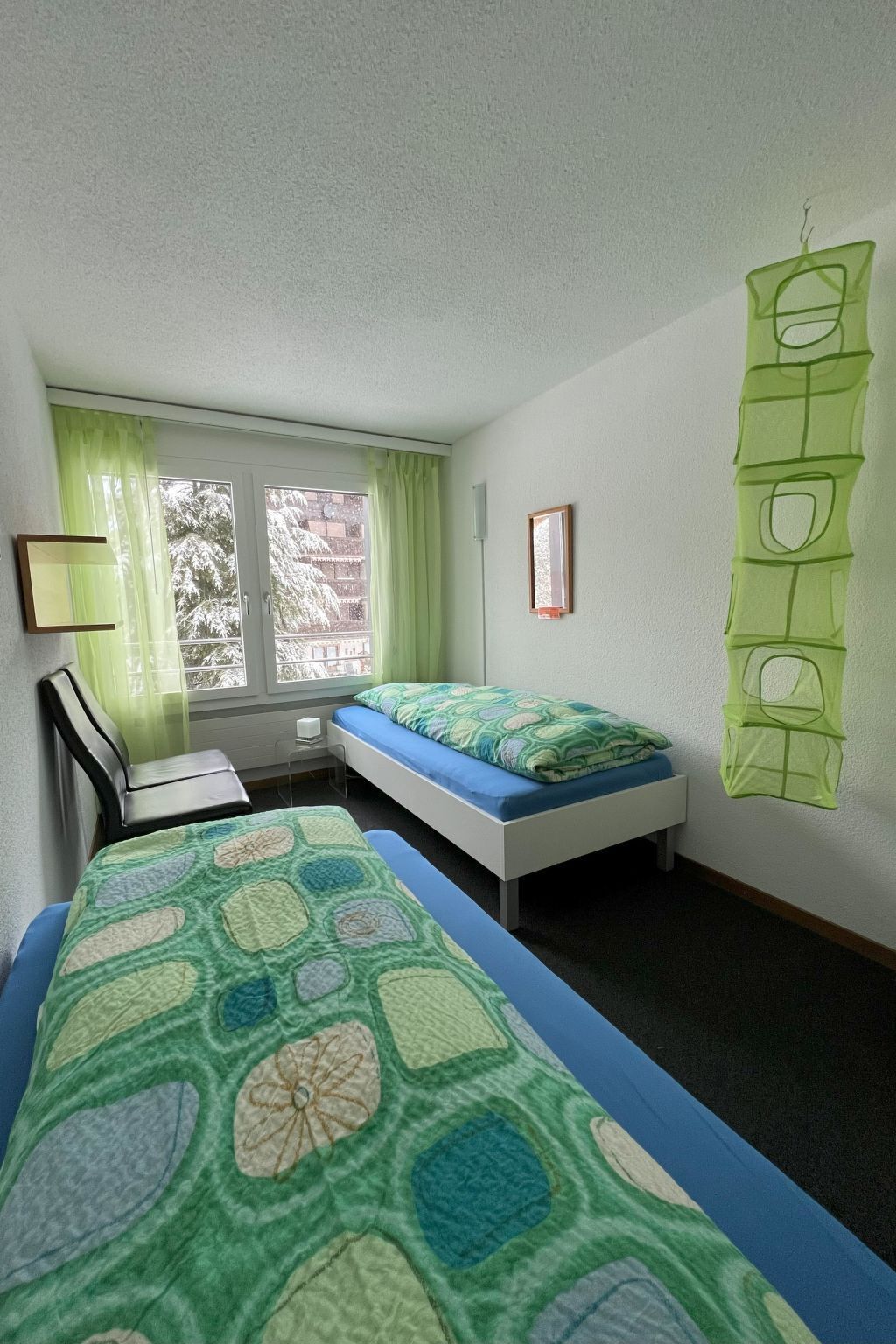 A room with two beds, a desk, a chair, and a window with curtains.