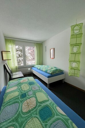 A room with two beds, a desk, a chair, and a window with curtains. - Beryll # 2 Appartement/Fewo, Dusche oder Bad, WC, 3 Schlafräume 6-Bett-Wohnung by Interhome (Lenk)