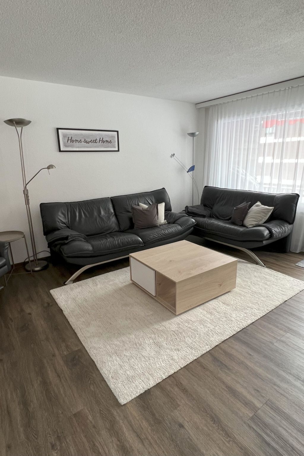 Ein modernes Wohnzimmer mit zwei schwarzen Ledersofas, einem Holztisch, einem weißen Teppich und einer Stehlampe.