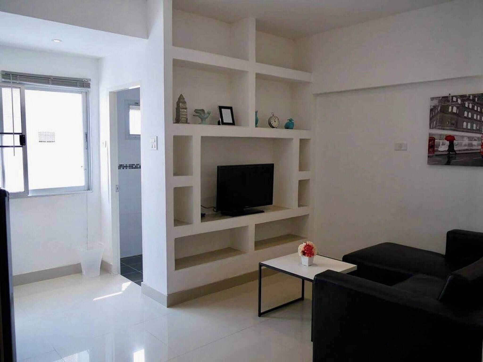 A modern living room with a flat-screen TV on a white shelf, a black sofa, and a small coffee table.