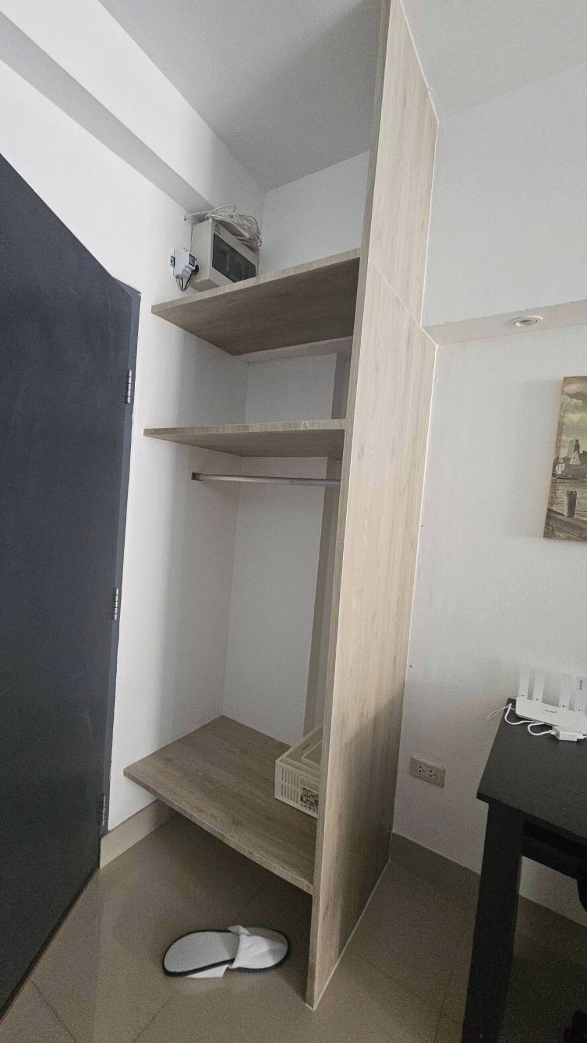 A room with a built-in wooden shelving unit, a door, and a pair of slippers on the floor.