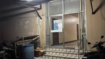 A building entrance with a metal gate, a blue barrel, and a scooter parked outside.