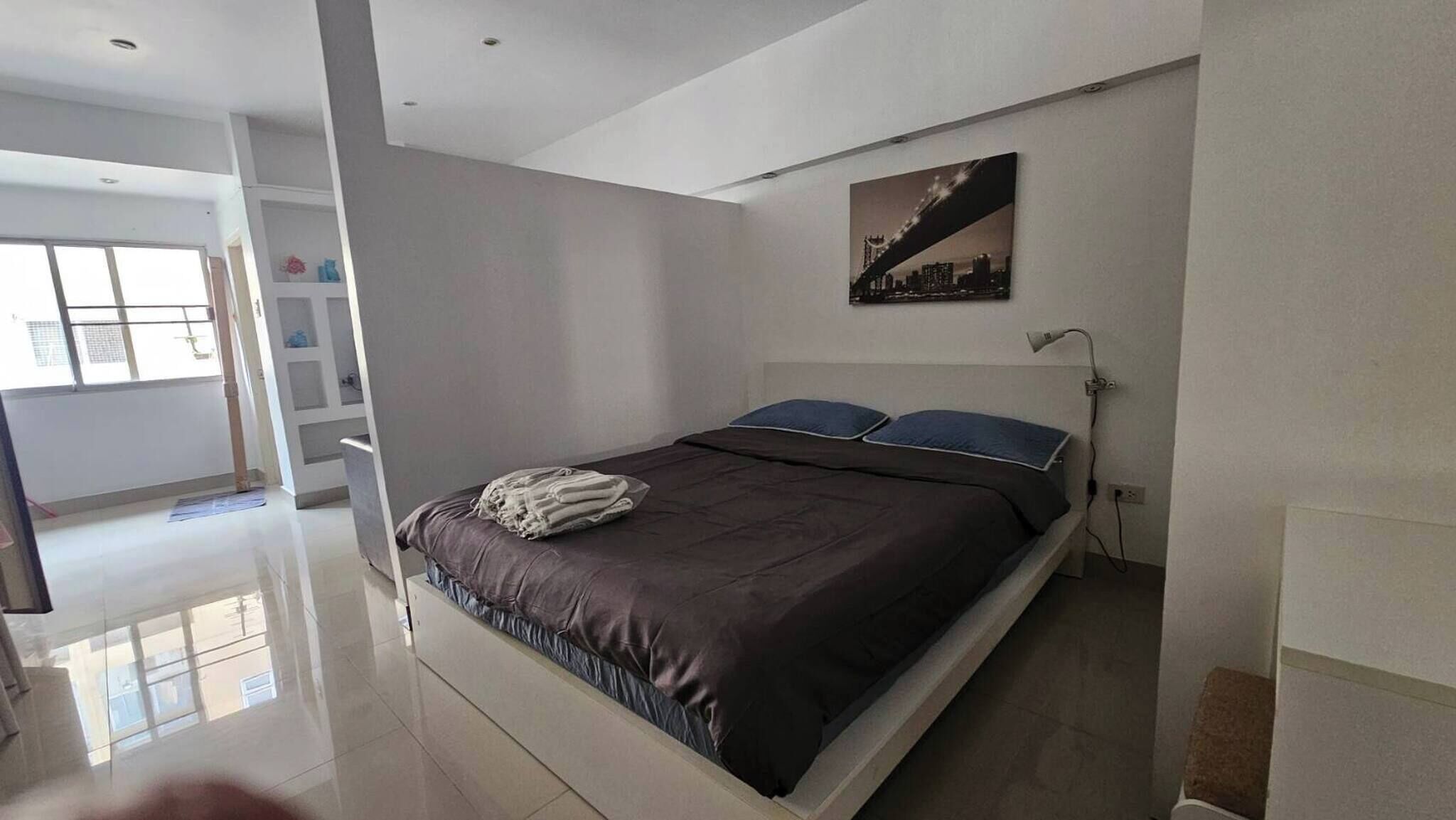 A modern bedroom with a bed, a nightstand, a lamp, and a cityscape painting on the wall.