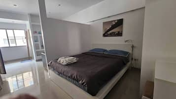 A modern bedroom with a bed, a nightstand, a lamp, and a cityscape painting on the wall.
