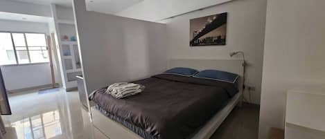 Un dormitorio moderno con una cama, una mesita de noche, una lámpara y un cuadro de un paisaje urbano en la pared.