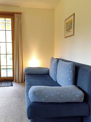A living room with a blue sofa, a window with curtains, and a framed picture on the wall. - Am Brüggli # 1 Appartement/Fewo, Dusche, WC, Erdgeschoß/Parterre 2-Bett-Wohnung by Interhome (Lenk)