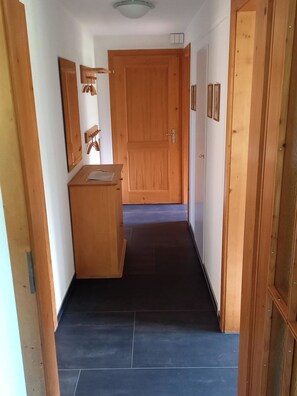 Ein Flur mit einer Holztür am Ende, einem kleinen Holztisch mit Stuhl und einem Spiegel an der Wand.