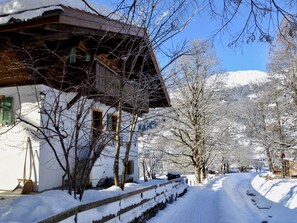 Eine verschneite Straße mit einem Gebäude auf der linken Seite, kahlbäumige Bäume und einem klaren Himmel.