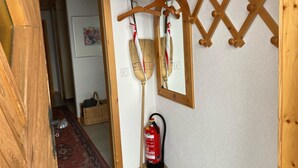 A hallway with a wooden floor, a fire extinguisher mounted on the wall, and a wooden coat rack with hangers. - Chalet Pulsatilla Appartement/Fewo, Dusche, WC Pulsatilla by Interhome (Rosswald)