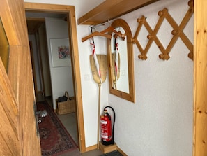 Ein Korridor mit Holzboden, einem an der Wand befestigten Feuerlöscher und einem Holz-Kleiderständer mit Kleiderbügeln.