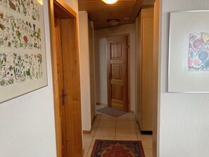 A hallway with wooden doors, a patterned rug, and a framed botanical illustration on the wall. - Chalet Pulsatilla Appartement/Fewo, Dusche, WC Pulsatilla by Interhome (Rosswald)