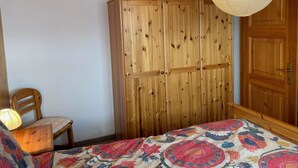 A bedroom with a wooden wardrobe, a bed with a colorful bedspread, a wooden chair, and a hanging light fixture. - Chalet Pulsatilla Appartement/Fewo, Dusche, WC Pulsatilla by Interhome (Rosswald)