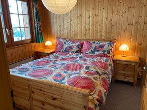 A wooden-paneled room with a bed, two bedside tables, and a window with curtains. - Chalet Pulsatilla Appartement/Fewo, Dusche, WC Pulsatilla by Interhome (Rosswald)