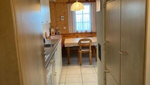 A narrow kitchen with wooden cabinets, a sink, a dining table with chairs, and a pendant light. - Chalet Pulsatilla Appartement/Fewo, Dusche, WC Pulsatilla by Interhome (Rosswald)