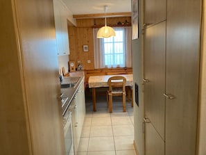 Eine schmale Küche mit Holzschränken, einem Spülbecken, einem Esstisch mit Stühlen und einer Pendelleuchte.