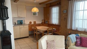 A cozy interior with a dining area, a sofa, a wooden table, and a black stove. - Chalet Pulsatilla Appartement/Fewo, Dusche, WC Pulsatilla by Interhome (Rosswald)