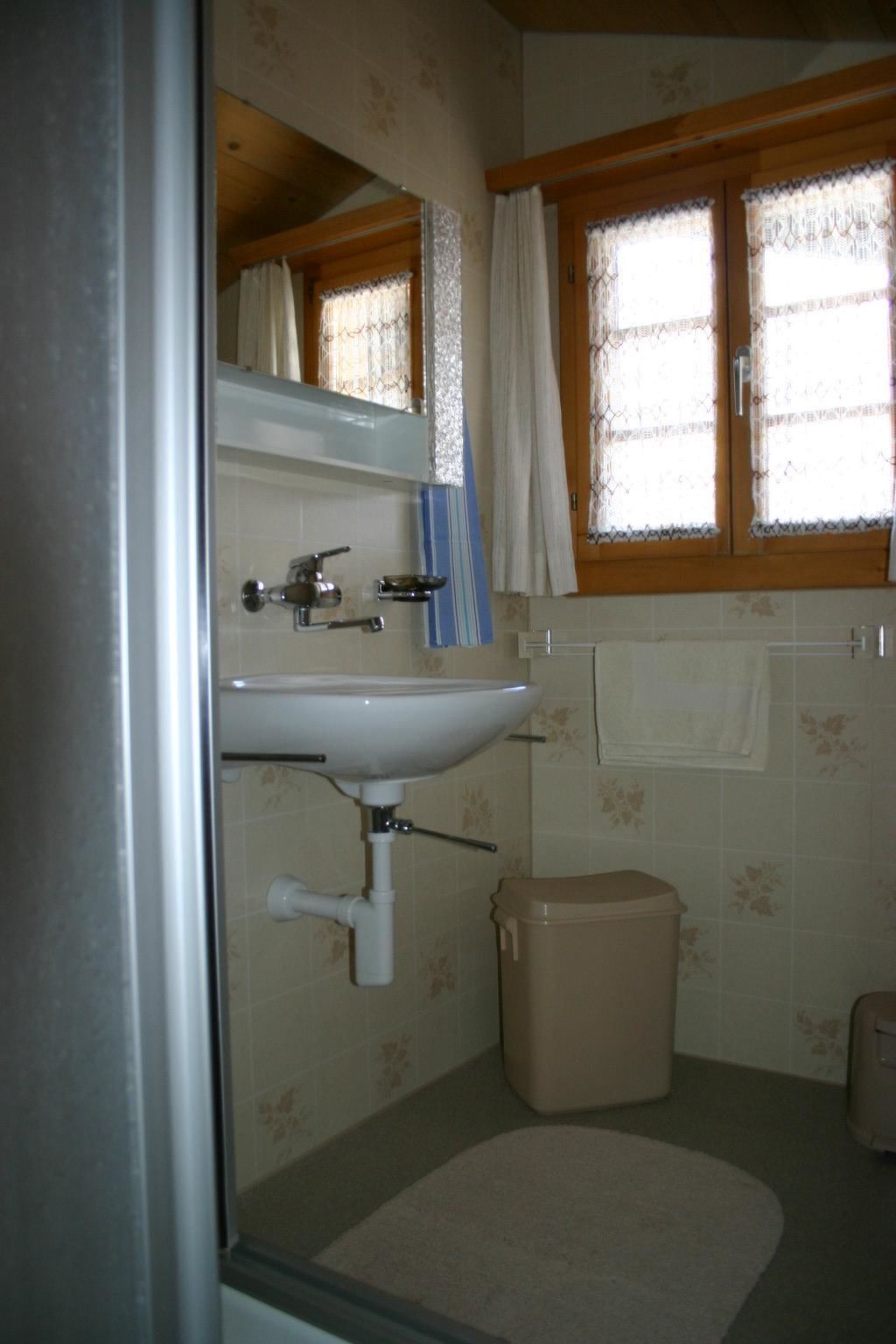 A bathroom with a sink, mirror, window with curtains, and a toilet.