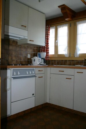 A kitchen with white cabinets, a stove, and a coffee maker. - Gletscherhorn # 2 Appartement/Fewo, Dusche oder Bad, WC, 1 Schlafraum by Interhome (Lenk)