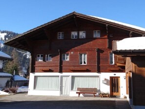 A two-story wooden building with a sloped roof, a front entrance, and a bench outside. - Gletscherhorn # 2 Appartement/Fewo, Dusche oder Bad, WC, 1 Schlafraum by Interhome (Lenk)