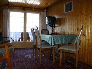 A dining area with a table set for four, wooden chairs, a patterned tablecloth, and a television mounted on the wall. - Gletscherhorn # 2 Appartement/Fewo, Dusche oder Bad, WC, 1 Schlafraum by Interhome (Lenk)