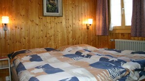 Puisilla paneeleilla verhoiltu huone, jossa on sänky, kaksi seinälle asennettua lamppua, ikkuna, jossa on verhot, ja patteri.