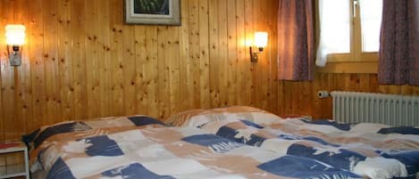 Ein Zimmer mit Holzwänden, einem Bett, zwei Wandlampen, einem Fenster mit Vorhängen und einer Heizung.
