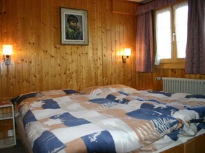 A wooden-paneled room with a bed, two wall-mounted lamps, a window with curtains, and a radiator. - Gletscherhorn # 2 Appartement/Fewo, Dusche oder Bad, WC, 1 Schlafraum by Interhome (Lenk)