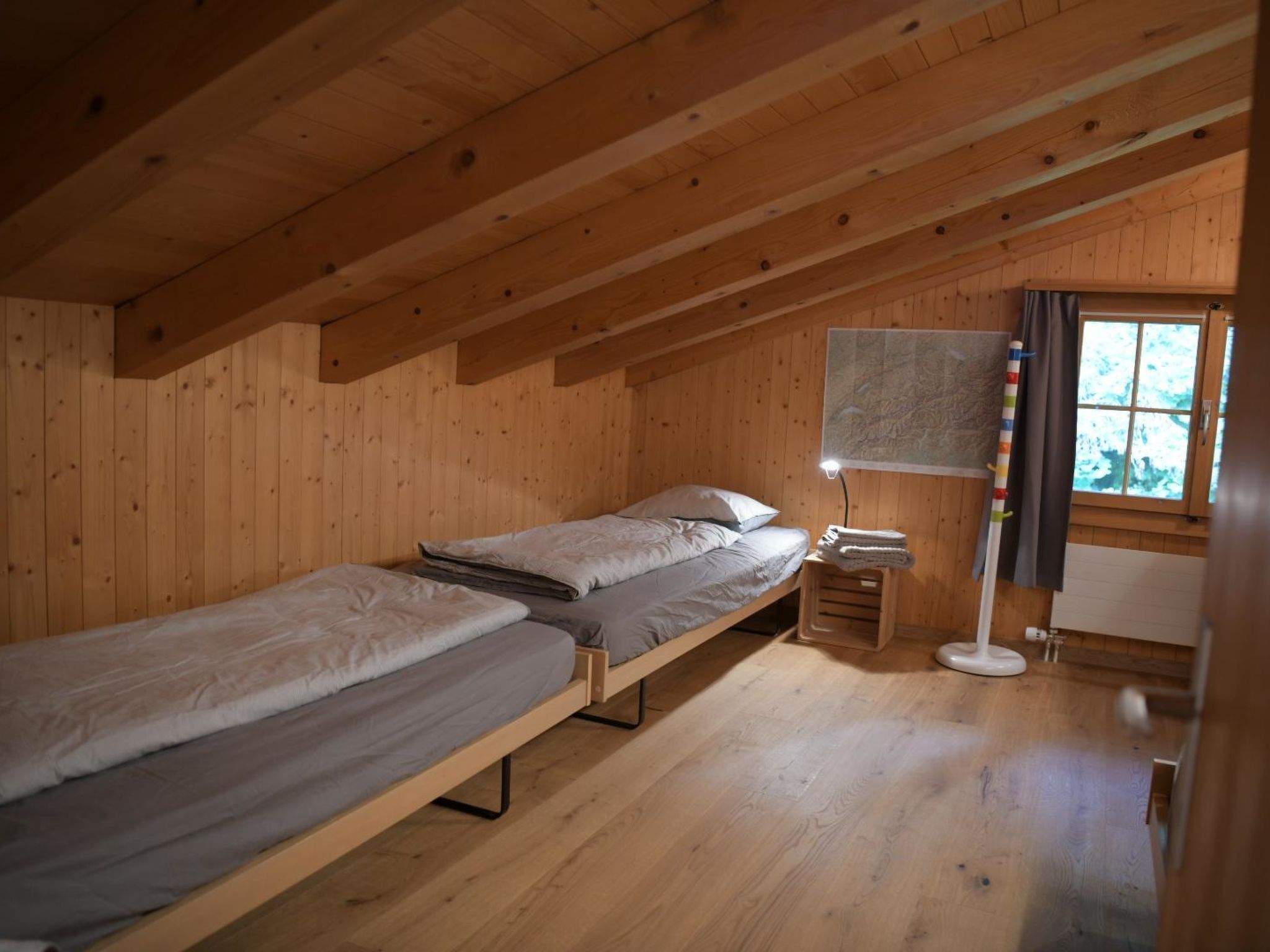 Een klein houten huisje met twee eenpersoonsbedden, een nachtkastje met een lamp en een raam met gordijnen.