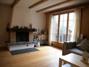 A living room with a fireplace, wooden flooring, a sofa, and a window with curtains. - Chalet Sunnebort Appartement/Fewo, Bad, WC, 2 Schlafräume 5-Bettwohnung by Interhome (Lenk)