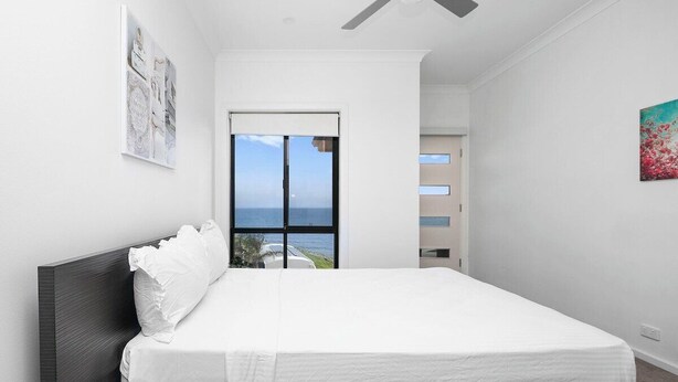 A bedroom with a large bed, a ceiling fan, a view of the sea through a window, and a door leading to another room. - Ocean View Home with Pool - Balcony - Sleeps 10 (Marino)