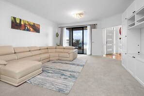 A modern living room with a beige sectional sofa, a patterned rug, and a large window with a view. - Ocean View Home with Pool - Balcony - Sleeps 10 (Marino)