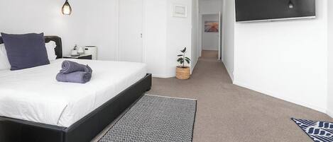 Un dormitorio con cama, mesita de noche, lámpara y televisor en la pared.