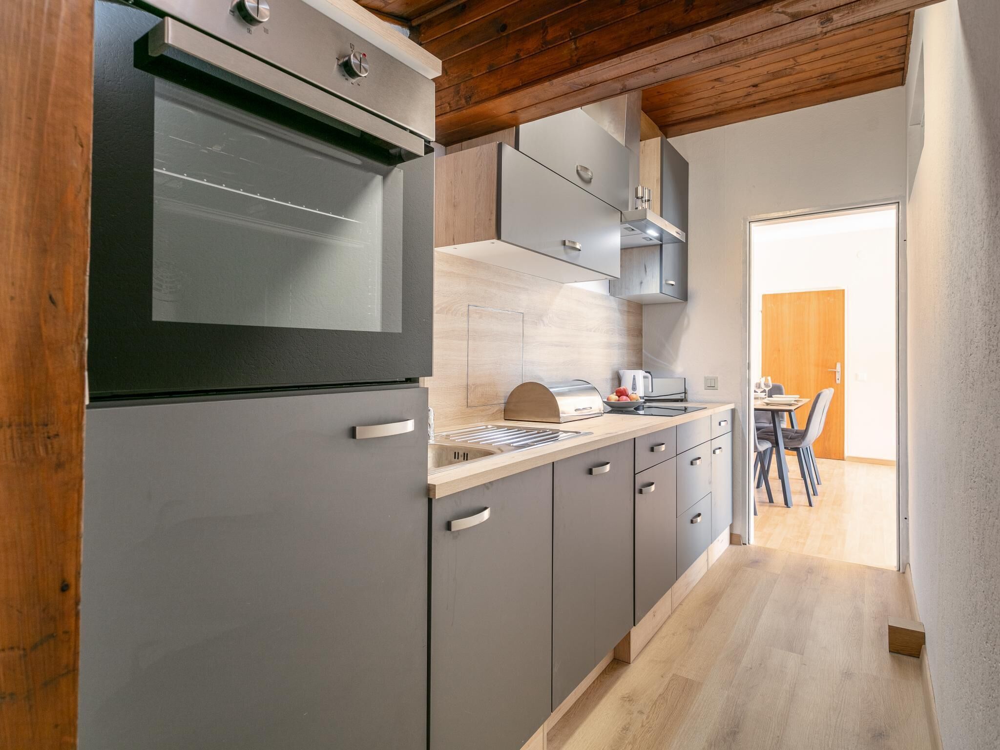 Une cuisine de taille réduite avec des meubles gris, un four encastré et un plafond en bois.