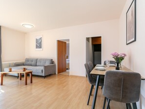 A modern living room with a grey sofa, a wooden coffee table, and a dining area with a table set for two.