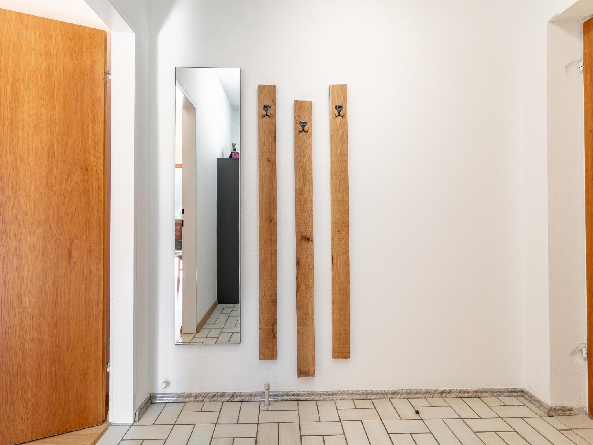 A hallway with a wooden door, a mirror, and three wooden planks on the wall.