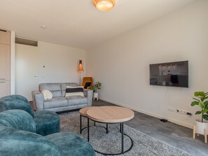 A modern living room with a grey sofa, teal armchairs, a wooden coffee table, and a TV mounted on the wall. - Apartment with terrace by the harbor of Kortgene (Kortgene)