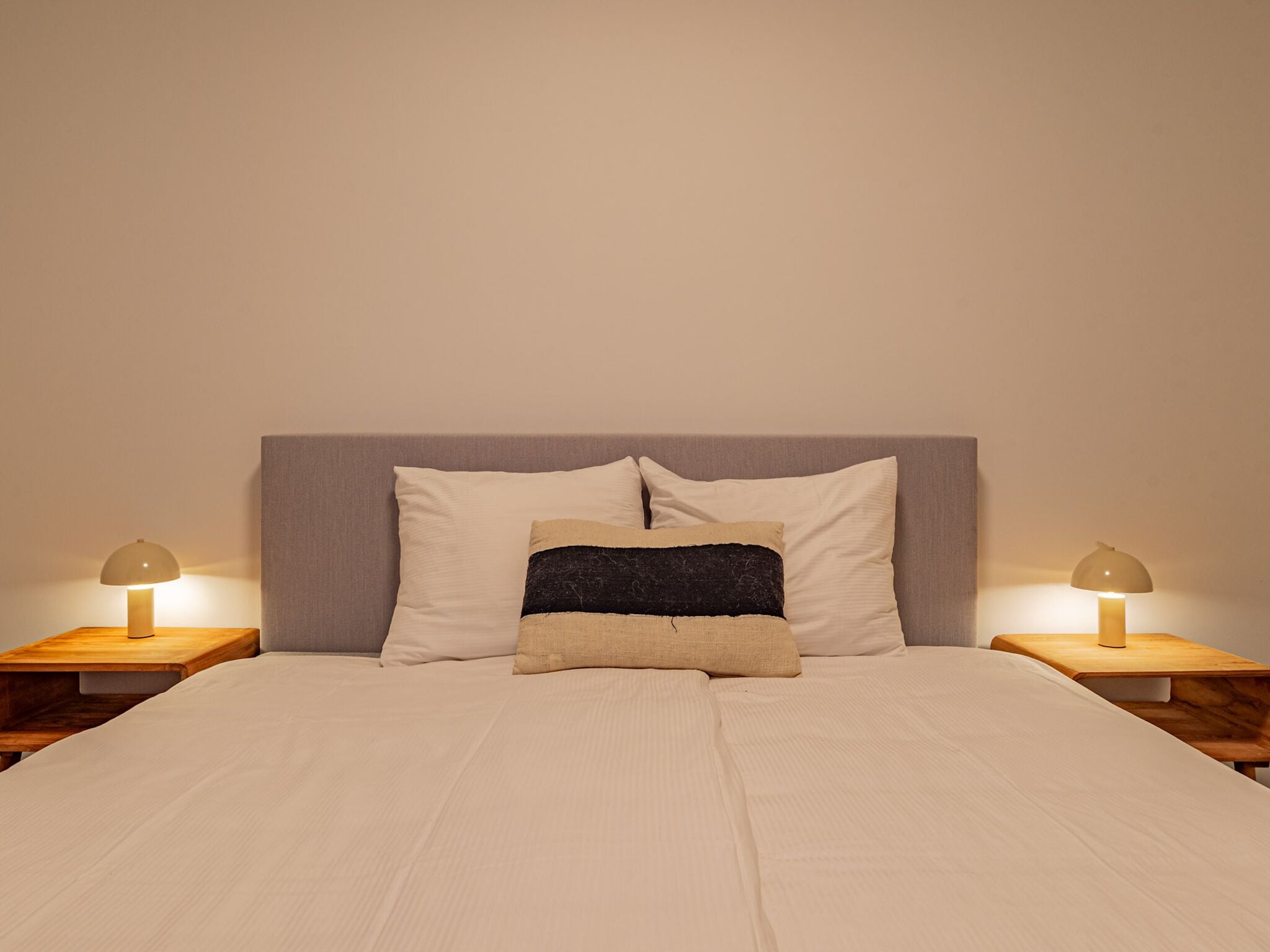 A bed with a headboard, two bedside tables, and two lamps.