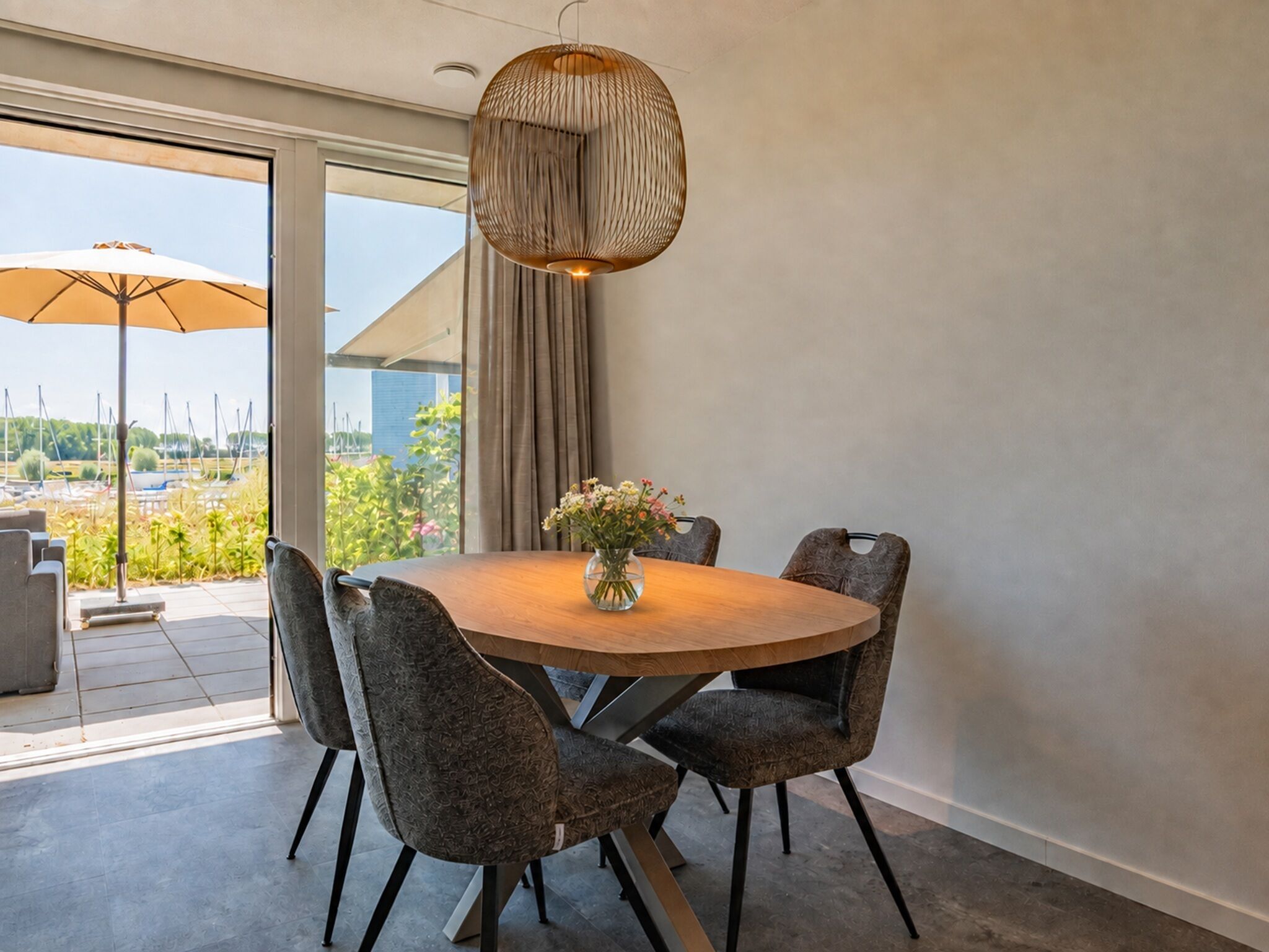 Een moderne eetruimte met een ronde tafel, vier stoelen, een vaas met bloemen en een hanglamp.