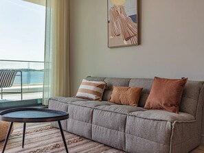 A grey sofa with striped and solid cushions, a small round table, and a view of the sea through large windows. - Luxury villa by the Veerse Meer (Kamperland)