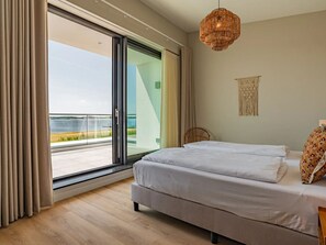 A bedroom with a bed, a wicker chandelier, a view of the sea, and a macrame wall hanging. - Luxury villa by the Veerse Meer (Kamperland)