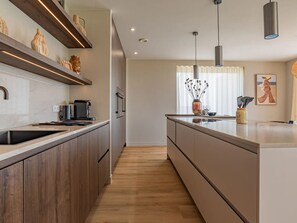 A modern kitchen with a central island, wooden cabinets, and pendant lighting. - Luxury villa by the Veerse Meer (Kamperland)