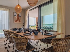 A dining area with a large table set for six, surrounded by wicker chairs, with a view of the outdoors through large windows. - Luxury villa by the Veerse Meer (Kamperland)