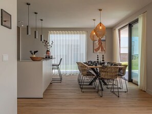 A modern kitchen with a dining area, featuring a large window, a dining table with chairs, and pendant lighting. - Luxury villa by the Veerse Meer (Kamperland)