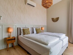 Una camera d'albergo con un letto, lampade sui comodini, un condizionatore d'aria a muro, un elemento decorativo e una finestra con tende.