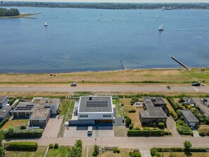 An aerial view of a modern building complex with a parking area, adjacent to a calm body of water with sailboats. - Luxury villa by the Veerse Meer (Kamperland)