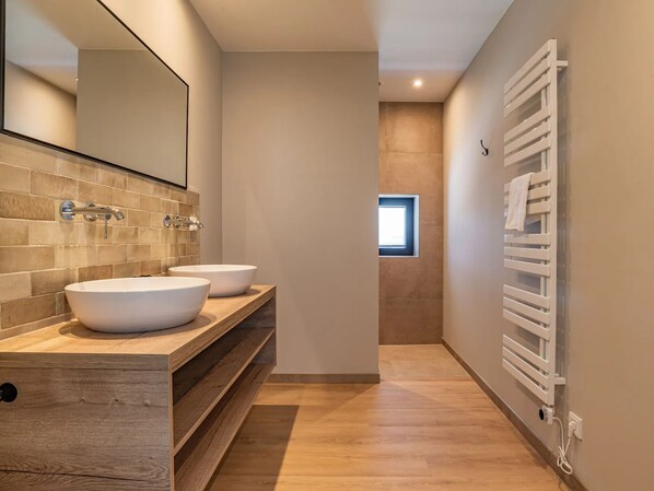 Een moderne badkamer met twee wastafels, een houten wastafelmeubel, een grote spiegel en een handdoekrek.