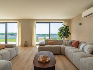 A spacious living room with a large sectional sofa, a coffee table, and a view of a lake. - Luxury villa by the Veerse Meer (Kamperland)