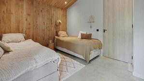 A bedroom with two beds, wooden ceiling, a white door, and a small bedside table. - Vacation home near the North Sea beach. (Kamperland)